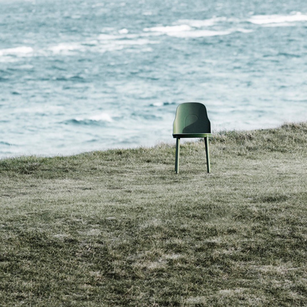 Green modern chair on grass by a coastal landscape, showcasing minimalist design and natural colors.