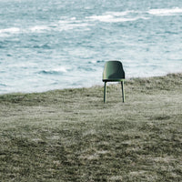 Green modern chair on grass by a coastal landscape, showcasing minimalist design and natural colors.