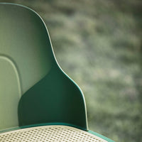 Green textured chair with a smooth back and perforated seat, set against a blurred natural background.