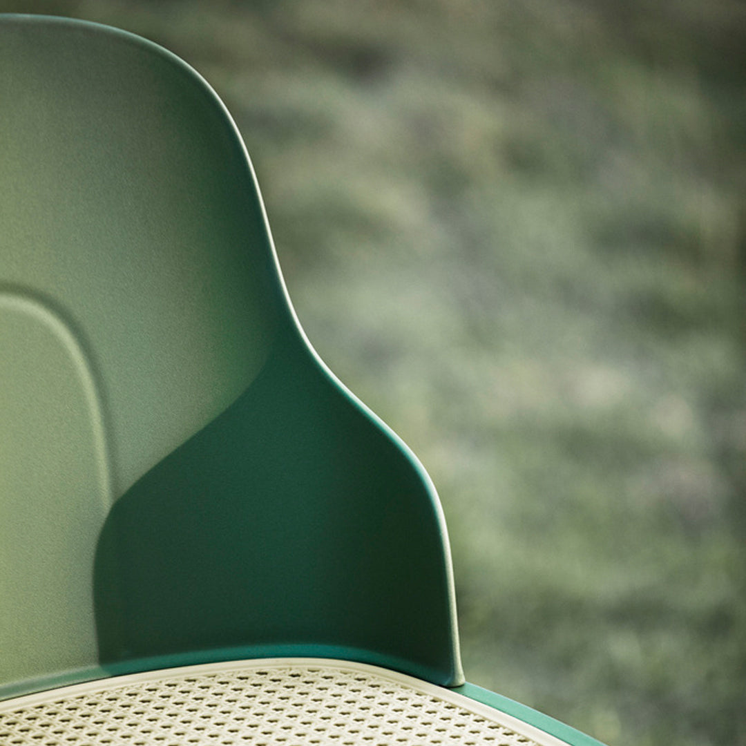 Green textured chair with a smooth back and perforated seat, set against a blurred natural background.