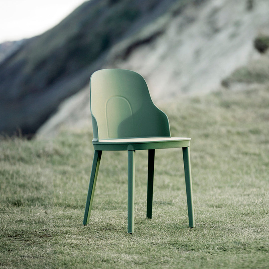 Solid green chair with a smooth surface and minimalist design, set against a natural grassy background.