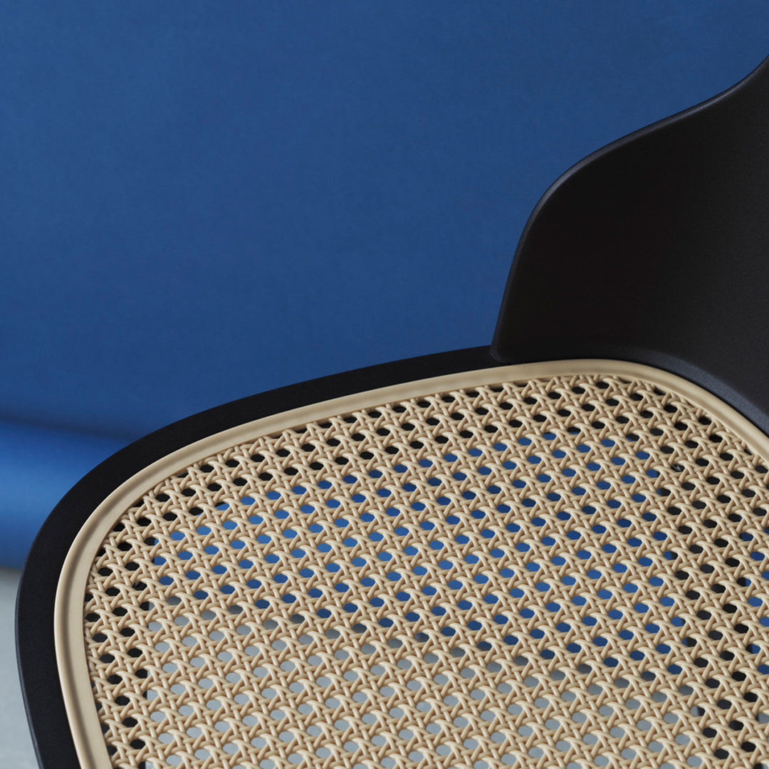 Black chair with a natural cane seat pattern against a deep blue background. Modern design with contrasting colors.