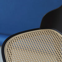 Black chair with a natural cane seat pattern against a deep blue background. Modern design with contrasting colors.