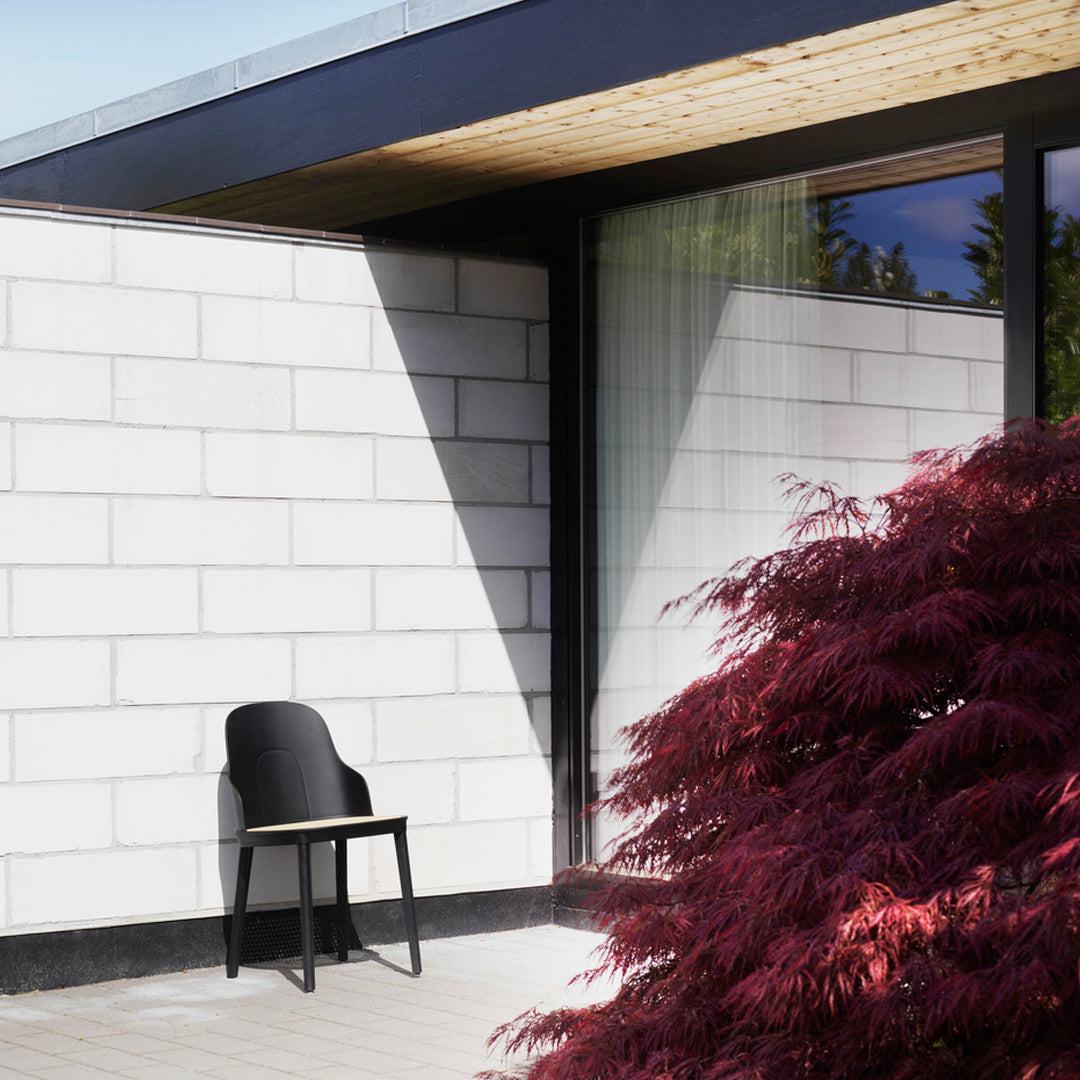 Black chair set against a white wall and vibrant red foliage, showcasing a modern design and contrasting colors.