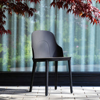 Modern black chair against a backdrop of green foliage and sheer curtains, showcasing sleek lines and minimalist design.