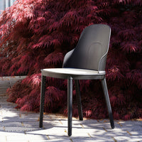 Black modern chair against vibrant red foliage. Sleek design with a smooth finish and minimalist aesthetic.
