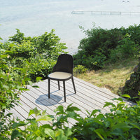 Black chair with cream seat cushion, set against lush green foliage and a serene waterfront backdrop.
