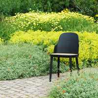 Black chair with a natural wood seat, set against vibrant yellow flowers and lush green foliage. Perfect for outdoor decor.