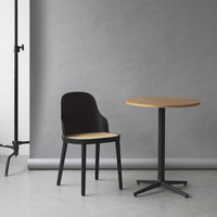 Black chair with light wood seat beside a round wooden table with a black base, set against a muted gray backdrop.