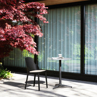 Black chair and glass table set against a backdrop of red foliage and sheer curtains, featuring a modern outdoor design.