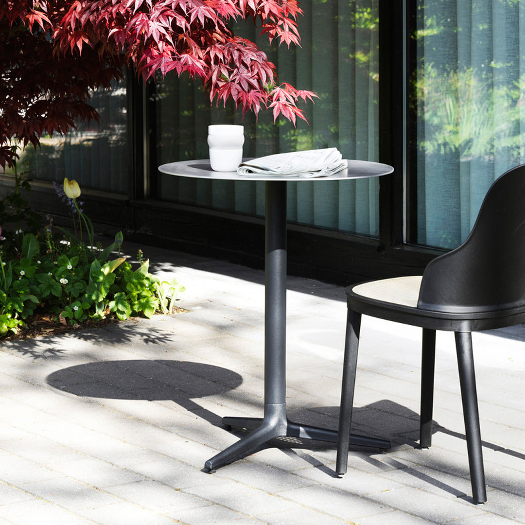 Black round table with a sleek design, set against a backdrop of vibrant green and red foliage. Perfect for outdoor use.