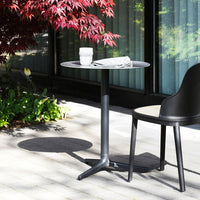 Black round table with a sleek design, set against a backdrop of vibrant green and red foliage. Perfect for outdoor use.