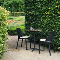 "Elegant black chairs with cream cushions around a sleek round table, set against lush greenery."
