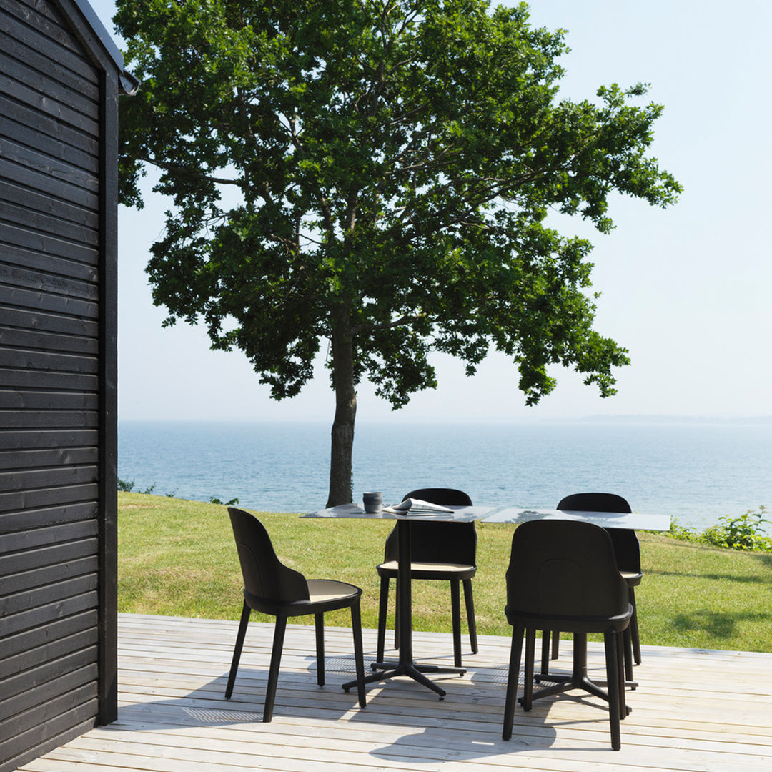 "Stylish black outdoor dining set on a wooden deck, surrounded by lush green grass and bright blue water."