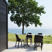 "Stylish black outdoor dining set on a wooden deck, surrounded by lush green grass and bright blue water."