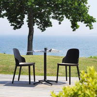 Black dining set with sleek, minimalist design, paired with a round tabletop, against a serene outdoor backdrop.