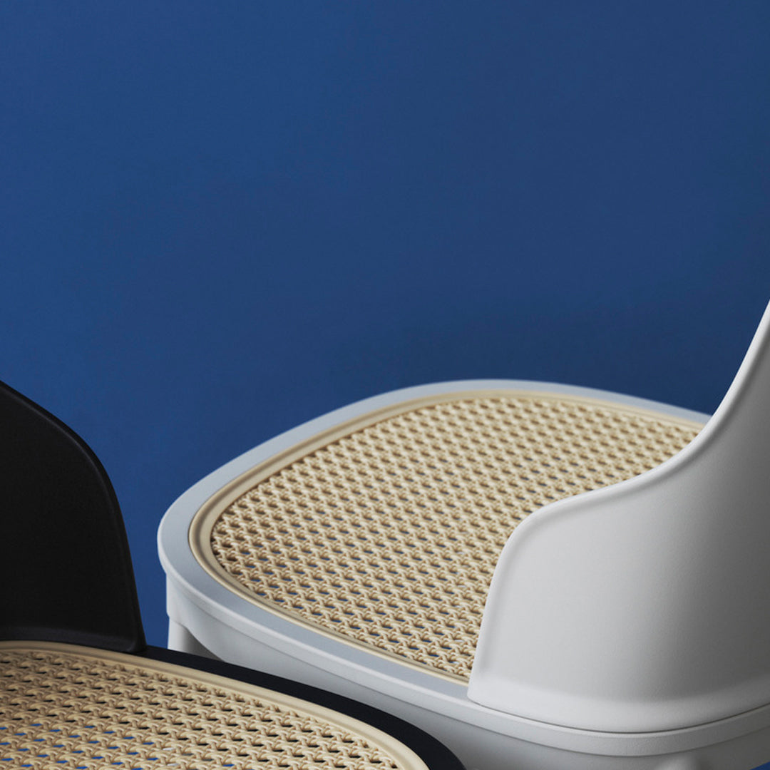 White and black chairs with woven cane seats, set against a vibrant blue background, showcasing modern design.