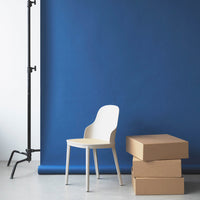 White chair with a smooth finish against a deep blue backdrop, complemented by stacked brown boxes.