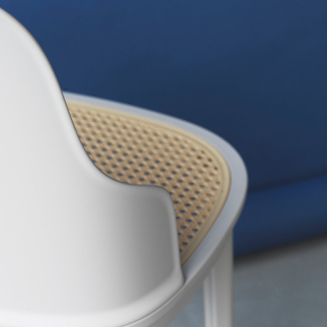 White chair with a natural cane seat pattern against a textured blue background. Casual and modern design.