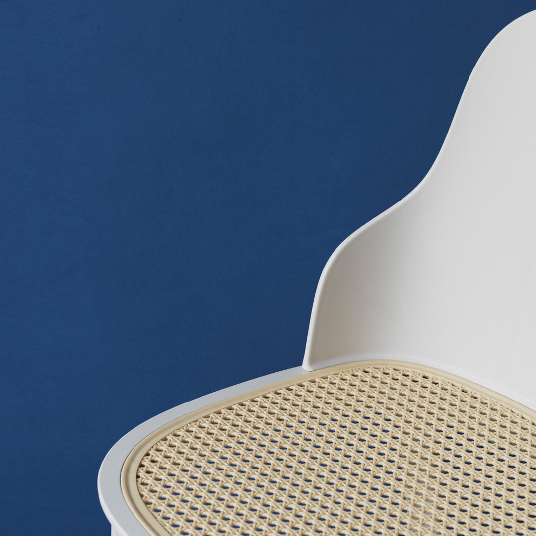 White chair with a natural cane seat against a deep blue background. Simple, modern design with earthy tones.