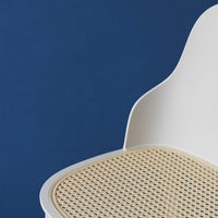 White chair with a natural cane seat against a deep blue background. Simple, modern design with earthy tones.