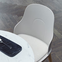 Light gray modern chair with a smooth finish and a soft beige seat cushion, set against a dark wood floor.