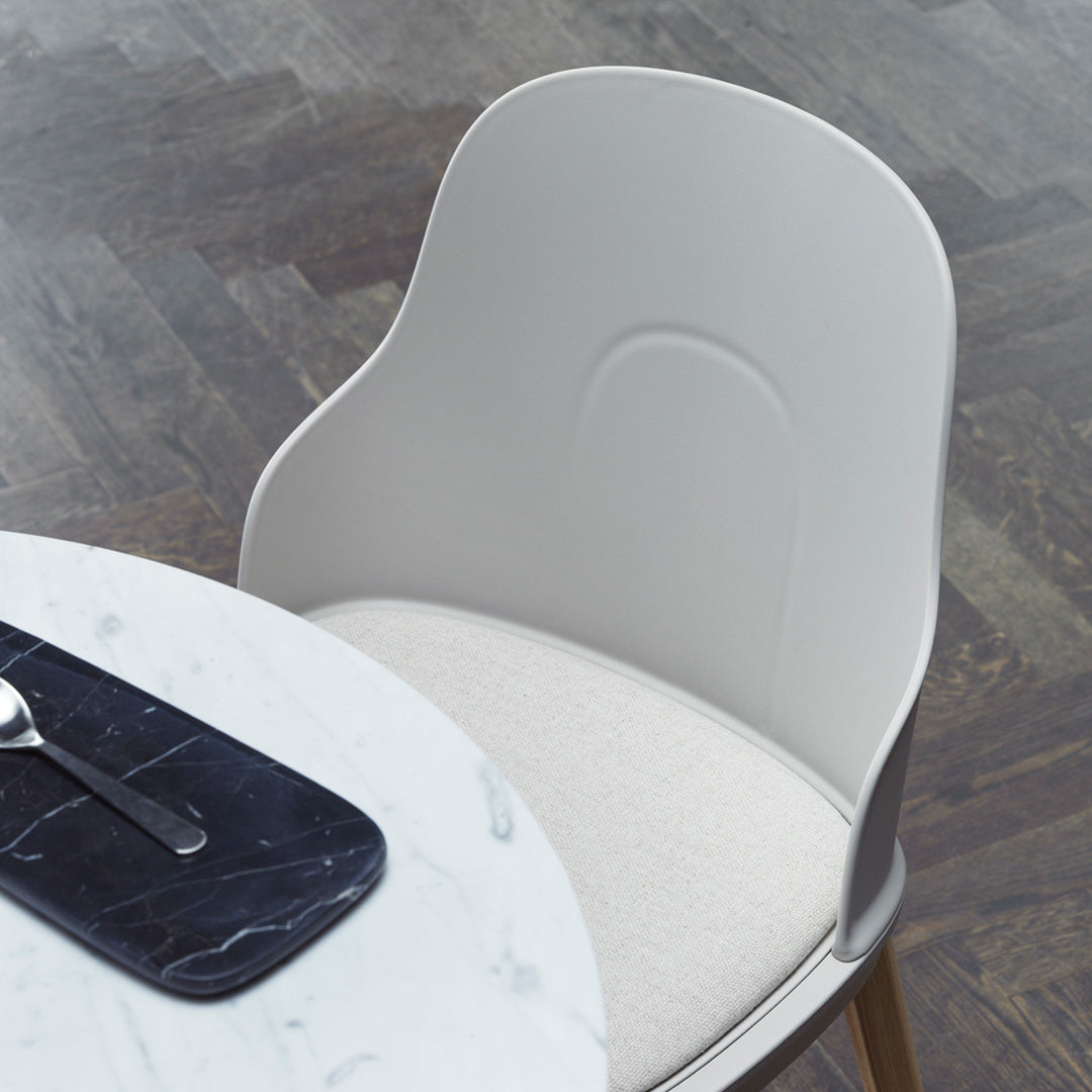 Light gray modern chair with a smooth finish and a soft beige seat cushion, set against a dark wood floor.
