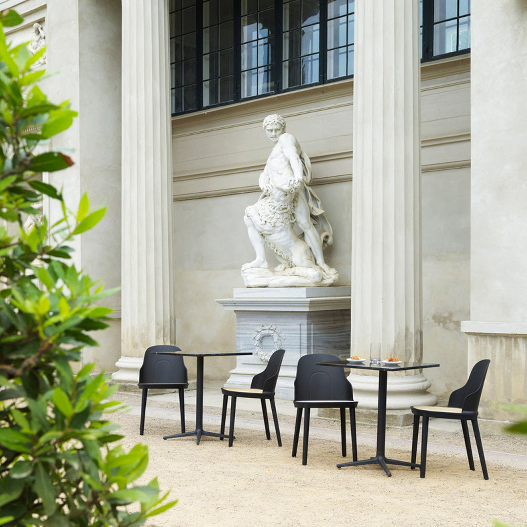 Black outdoor chairs and tables against a neutral stone backdrop with lush greenery. Elegant, modern design.