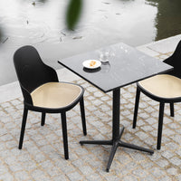 Black and tan dining chairs with a black marble tabletop, set on a gray cobblestone patio by a water feature.
