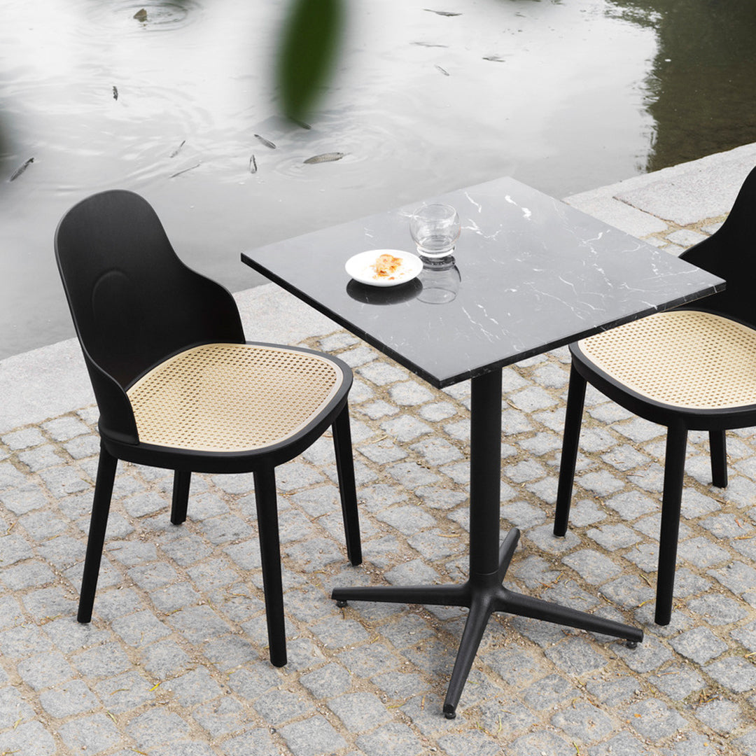 Black and tan dining chairs with a black marble tabletop, set on a gray cobblestone patio by a water feature.