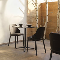 Modern black dining chairs with sleek design, paired with a round black tabletop in a natural light setting.