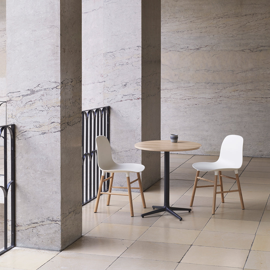 Modern white chairs with natural wood legs beside a round light wood table in a sleek, minimalist setting.