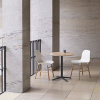 Modern white chairs with natural wood legs beside a round light wood table in a sleek, minimalist setting.