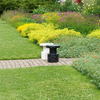 Black and white speckled garden stools on a stone path surrounded by vibrant yellow and green flowers.