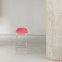 Pink bar stool with a smooth, curved seat and sleek chrome legs, set against a minimalist backdrop.