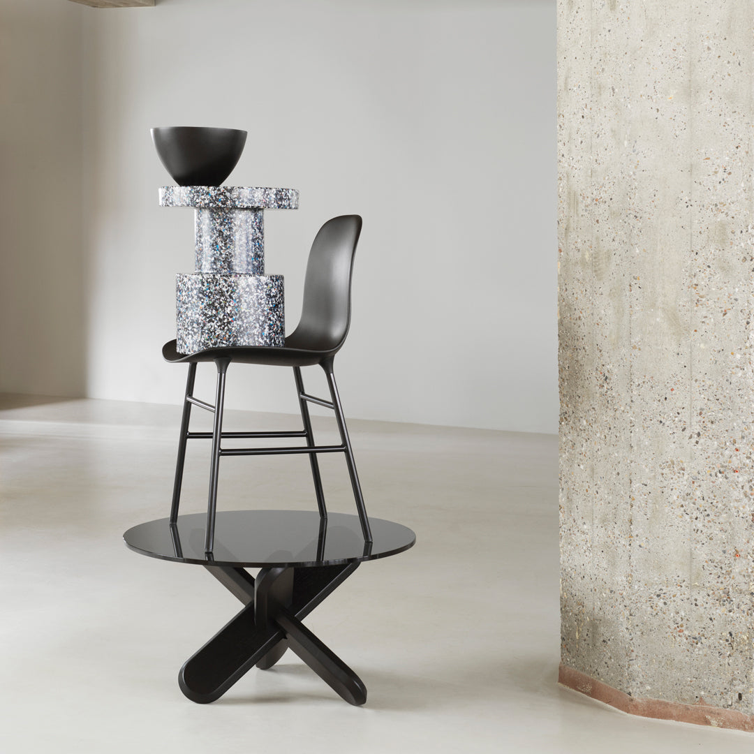 Black and white chair atop a sleek black table, complemented by a speckled gray and blue patterned pedestal.