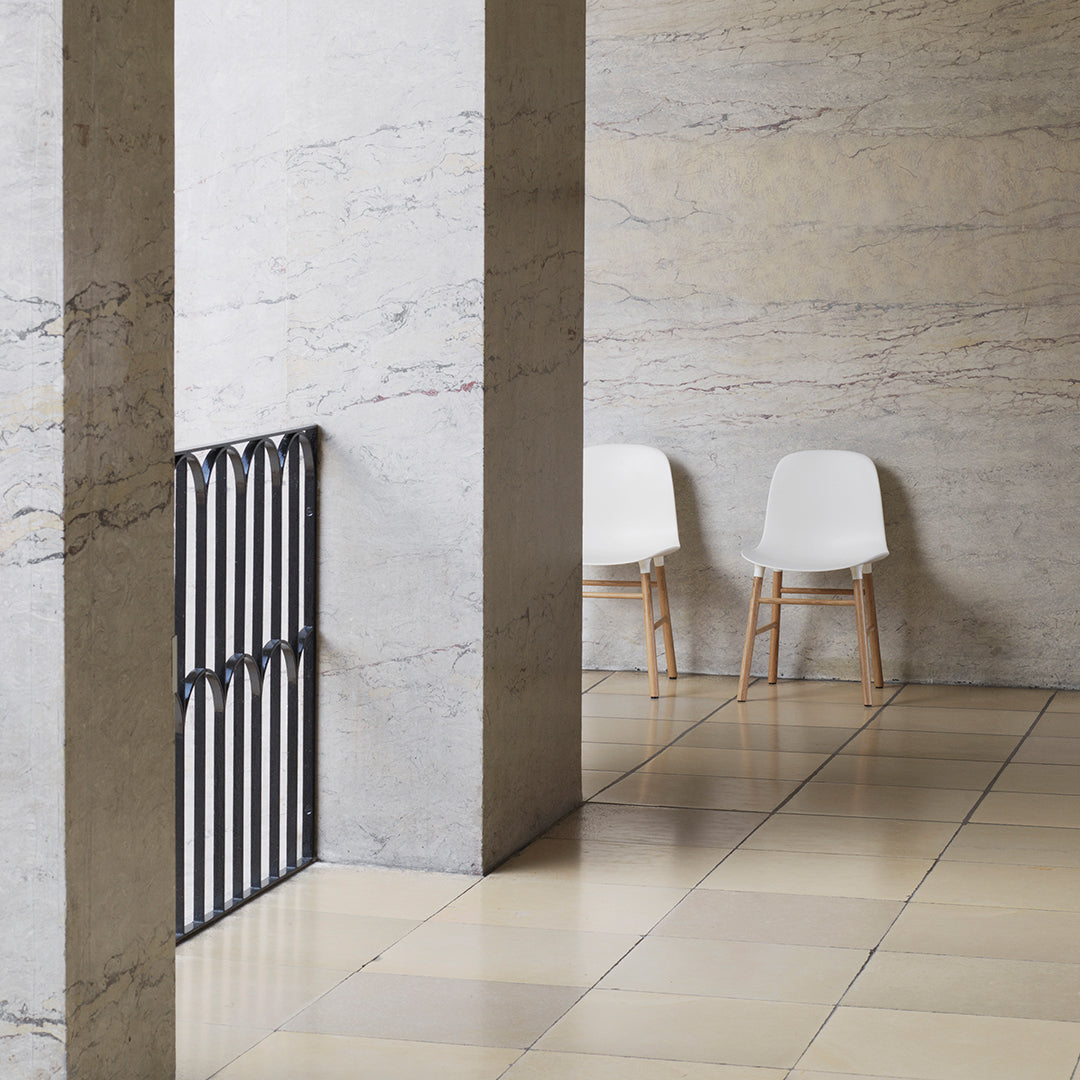 Minimalist white chairs against a light-toned marble wall and beige tiled floor, featuring soft neutral patterns.