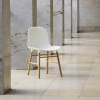 White chair with a smooth surface and natural wood legs, set against a minimalist stone backdrop.