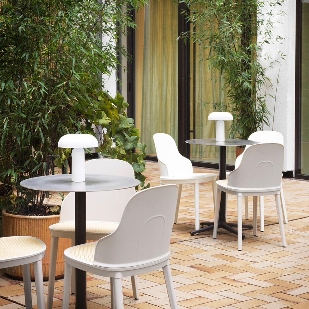 Modern white chairs paired with sleek gray tables, surrounded by green bamboo in a stylish outdoor setting.