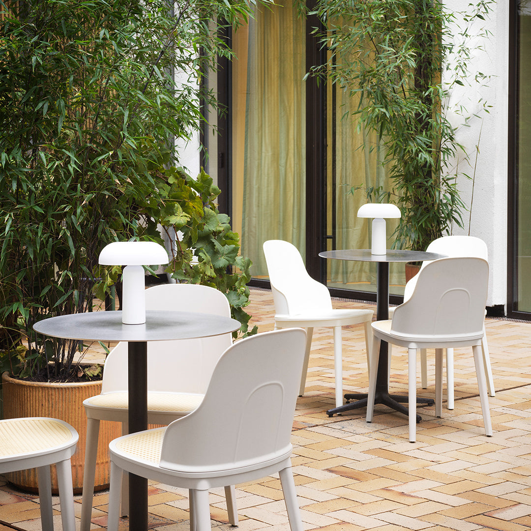 Light grey and white chairs around a black table, set against a green bamboo backdrop and warm brick flooring.