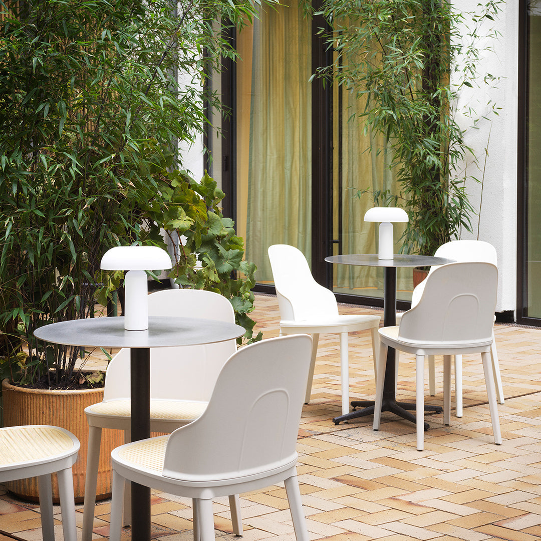Light grey and white chairs around a black table, set against a green bamboo backdrop and warm brick flooring.