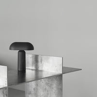 Modern black lamp on a sleek metallic surface against a light gray wall, showcasing a minimalist aesthetic.