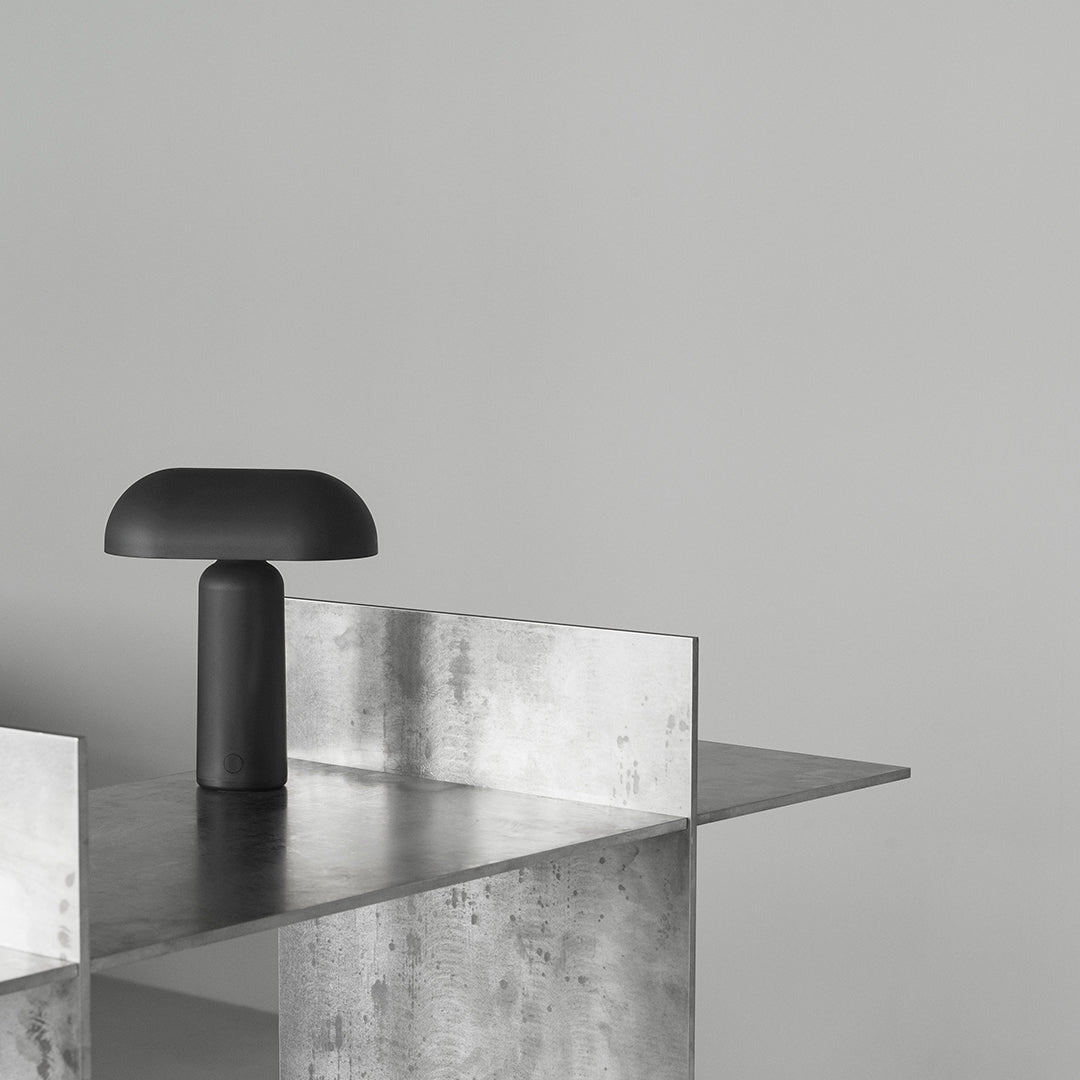Modern black lamp on a sleek metallic surface against a light gray wall, showcasing a minimalist aesthetic.