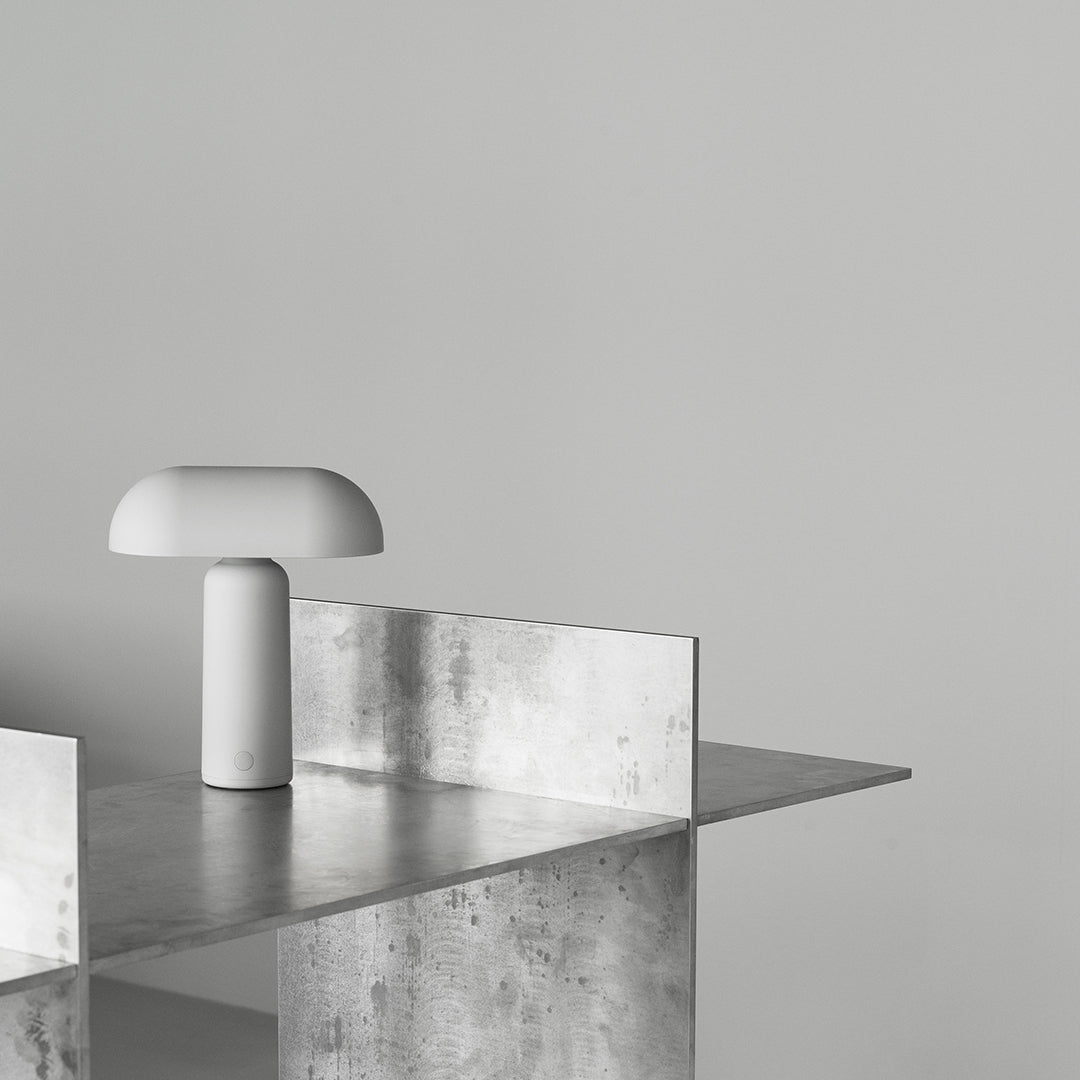 Modern minimalist lamp with a white finish on a sleek metallic tabletop against a soft gray background.