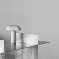 Modern minimalist lamp with a white finish on a sleek metallic tabletop against a soft gray background.