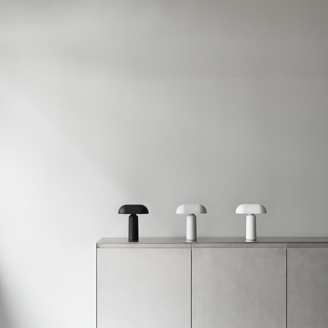 Three minimalistic lamps in black and white on a sleek gray cabinet, featuring smooth, modern shapes.
