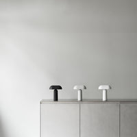Three minimalistic lamps in black and white on a sleek gray cabinet, featuring smooth, modern shapes.