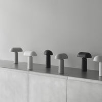 "Minimalist mushroom-shaped lamps in shades of white, gray, and black, arranged on a sleek, light gray surface."