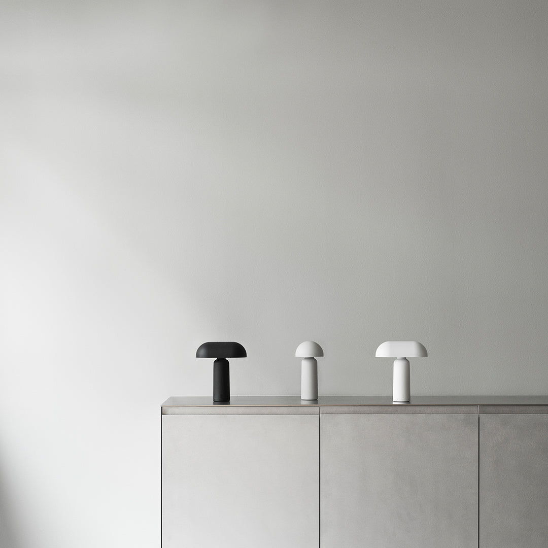 Three minimalist lamps in black, white, and grey, with smooth, curved shapes against a light grey wall.