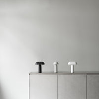 Three minimalist lamps in black, white, and grey, with smooth, curved shapes against a light grey wall.